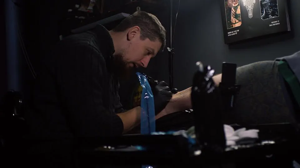 Void Tattoo meistars tetovē roku tumšā studijas telpā